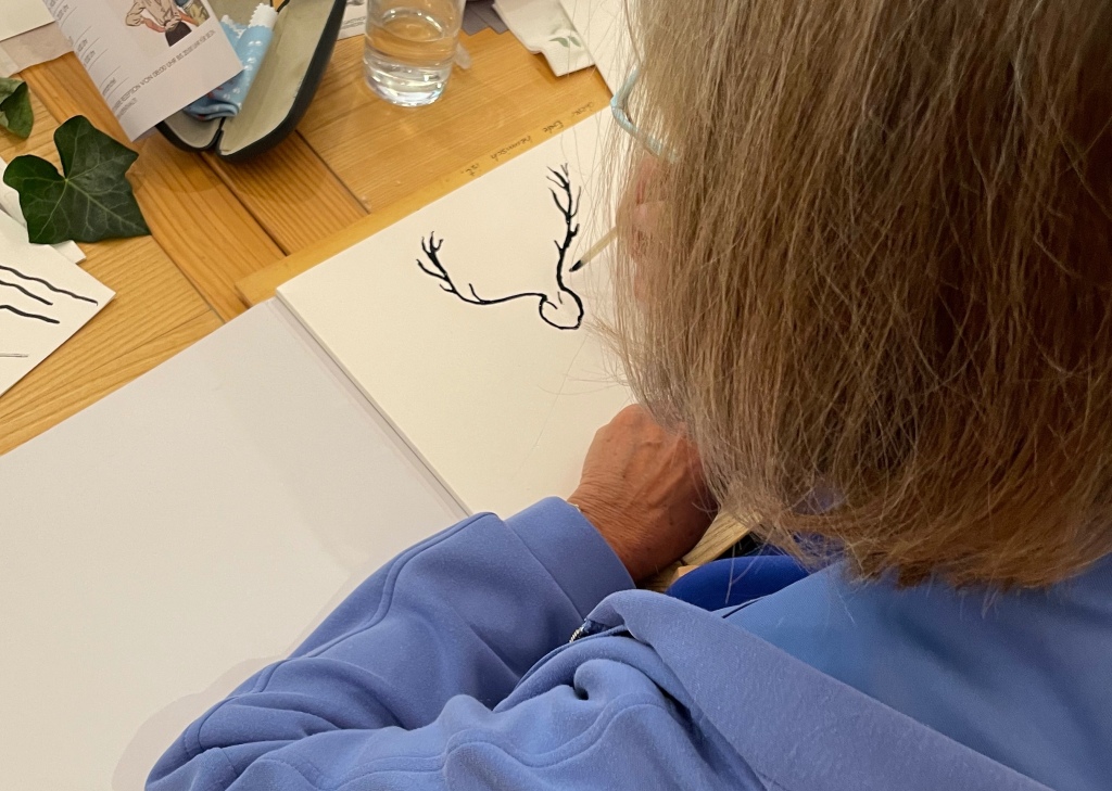 Person zeichnet mit Feder ein Hirschgeweih auf Papier